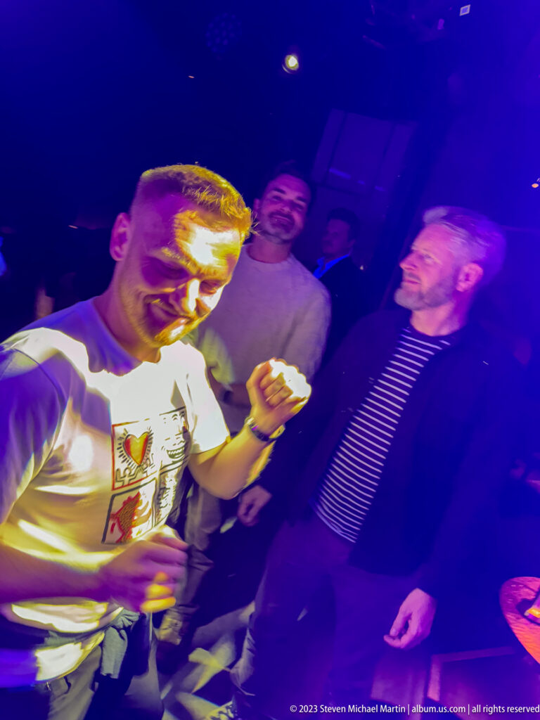 Man dancing in a nightclub under purple and blue lights, with several companions standing behind him.