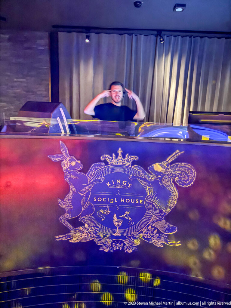 Man behind an illuminated King's Social House counter under red, purple, and blue lighting.