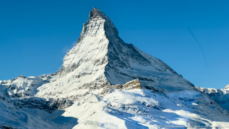 Close sunlit view of the snow-covered Matterhorn rising sharply against a deep blue sky.