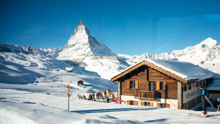 Timber chalet and small group of skiers in snow with the Matterhorn rising directly behind.
