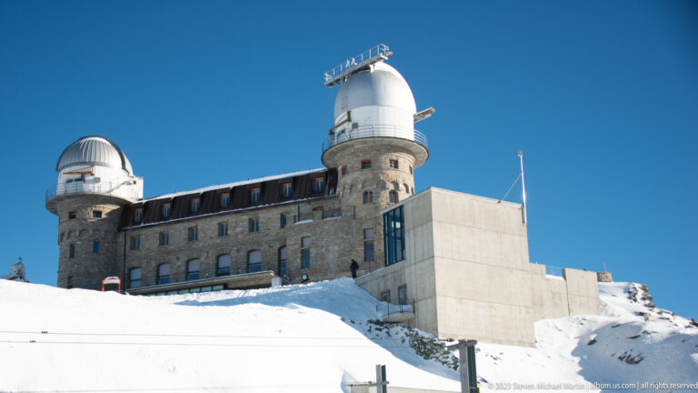 Side view of the 3100 Kulmhotel Gornergrat with stone facade, two observatory domes, and modern concrete addition.