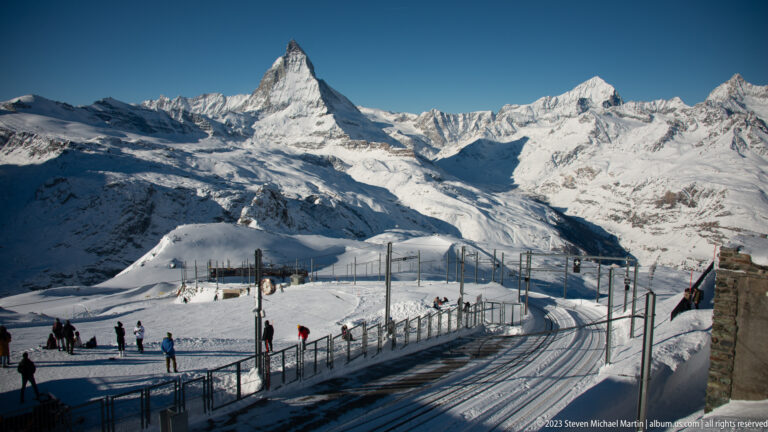 Curving Gornergrat railway tracks and catenary beneath the Matterhorn on a snowy mountain plateau.