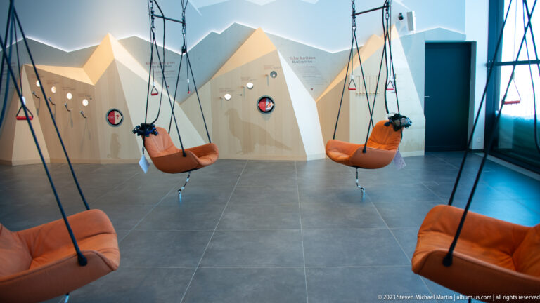 Orange suspended seats hanging from cables inside a bright mountain-themed interactive exhibit.