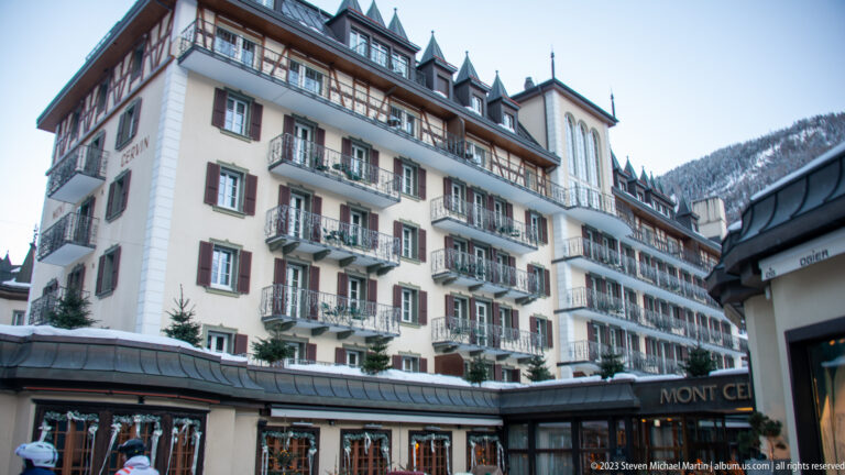 Mont Cervin Palace with balconies, shutters, dormers, and a corner tower above the snowy street.
