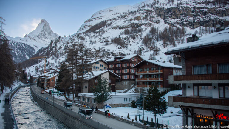 Matter Vispa flowing beside chalet buildings and a snowy street, with the Matterhorn visible beyond.