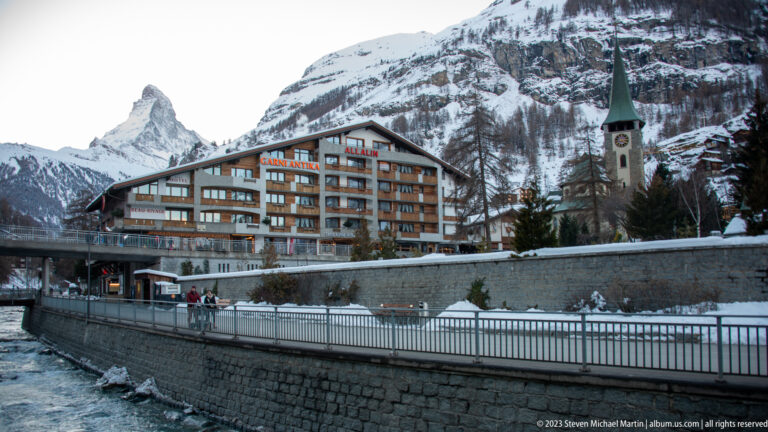 Hotel Antika and St. Mauritius Church beside the Matter Vispa, with the Matterhorn visible in the distance.