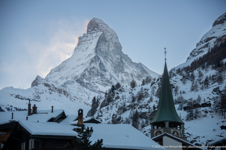 Matterhorn towering above the green spire of St. Mauritius Church and snow-covered village roofs.