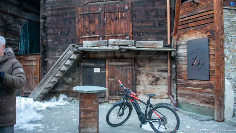 Weathered timber building with plank doors, rough beams, loading platform, and a bicycle in front.