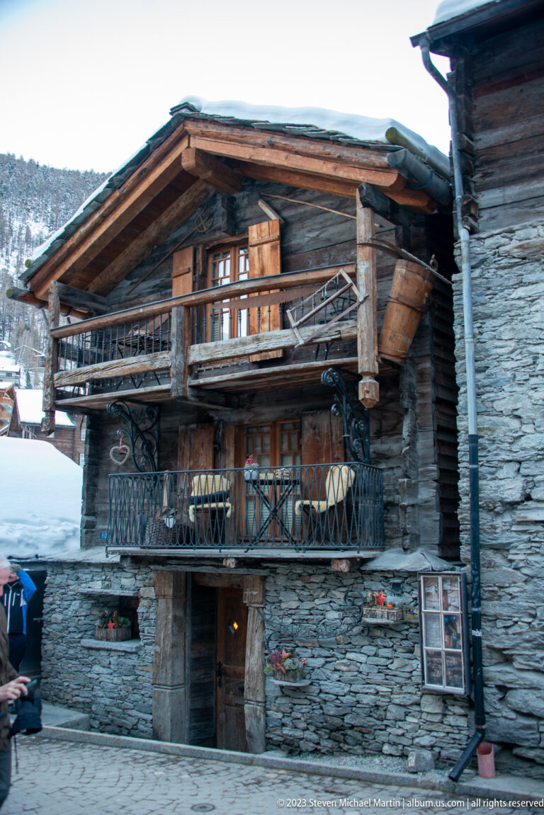 Historic timber chalet with broad balconies and a stone lower level beneath a snow-covered roof.