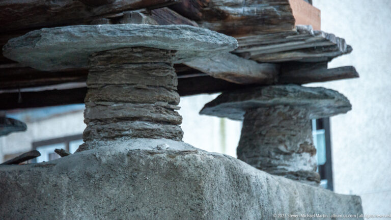 Close-up of stacked stone piers and flat stone discs supporting a raised timber structure.