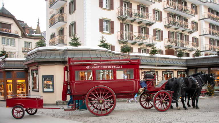 Red Mont Cervin Palace carriage with two black horses standing on a snowy street.