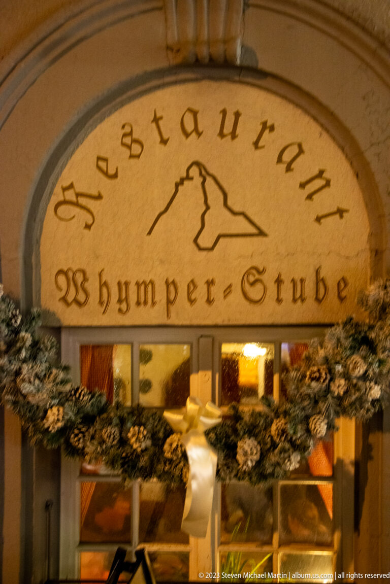 Arched sign reading Restaurant Whymper-Stube above a garland-decorated entrance.