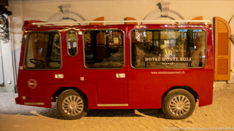 Small red Hotel Monte Rosa electric shuttle parked on a cobbled street at night.