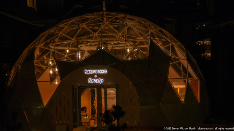 Illuminated geodesic dome pavilion at night with a NESPRESSO sign above the entrance.