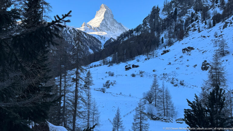 Matterhorn rising above a snowy valley with dark conifer forest beneath a clear blue sky.
