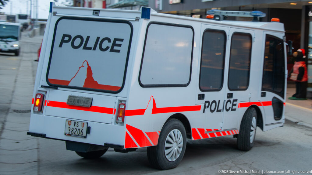 Compact white Zermatt police shuttle with red striping, Matterhorn graphic, and large POLICE lettering.