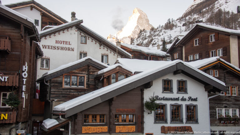 Hotel Weisshorn and Restaurant du Pont beneath snowy roofs, with the Matterhorn rising between the buildings.