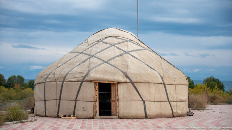 Large white yurt standing near the lakeshore.