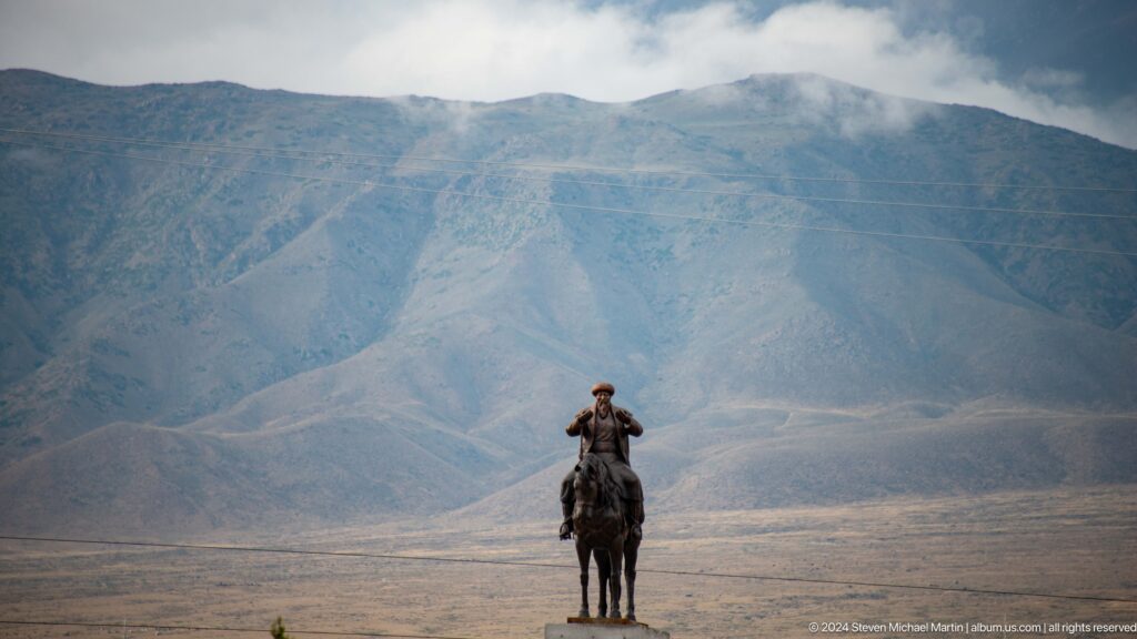 Horse rider crossing open plain below mountains.