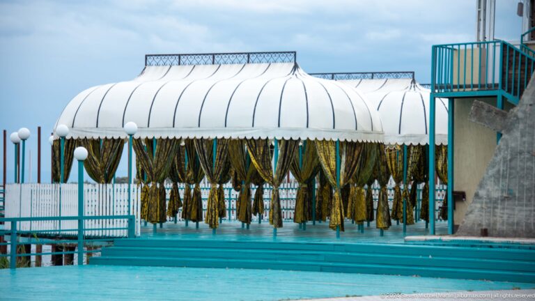 Covered lakeside structure hung with drying plants.