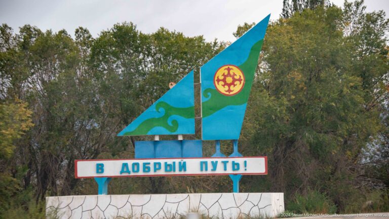 Kyrgyz flag sculpture above welcome lettering.