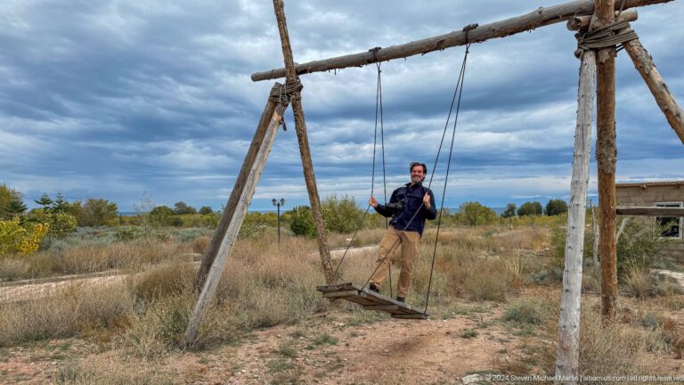 Person seated on a rustic wooden swing.