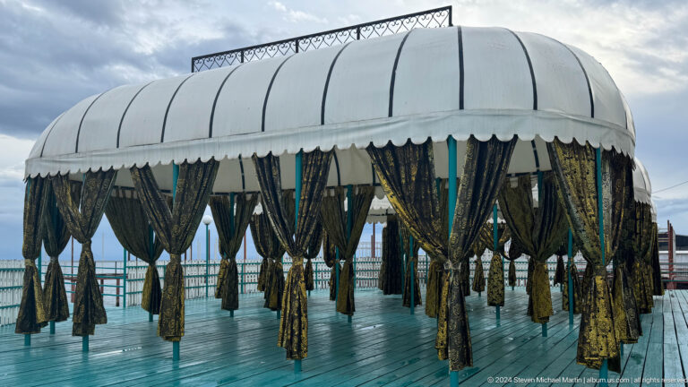 Covered pavilion with hanging plants near water.