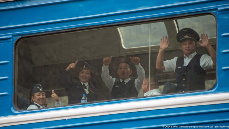 Uniformed passengers waving through train window.