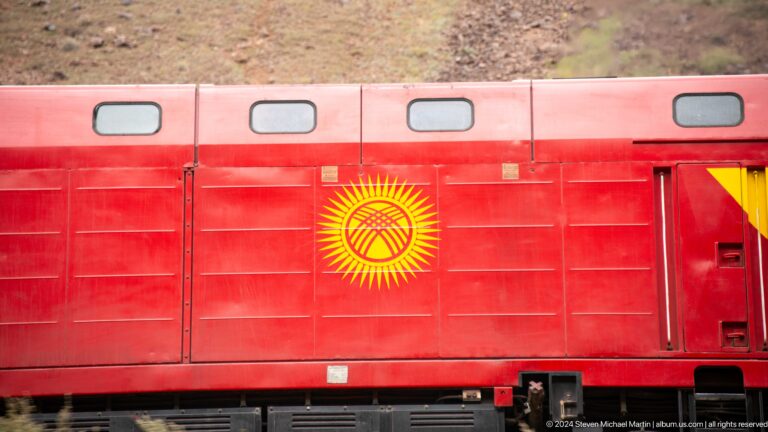 Red railcar painted with kyrgyz national emblem.