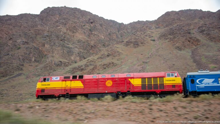 Red-and-yellow locomotive and carriage in hills.