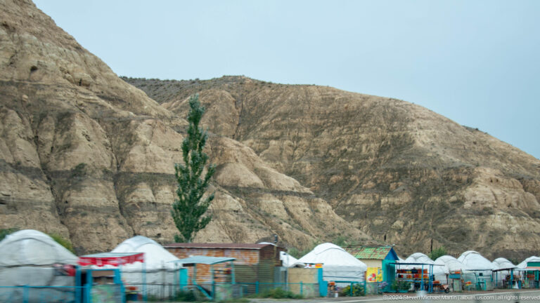 White yurts below sculpted tan cliffs.