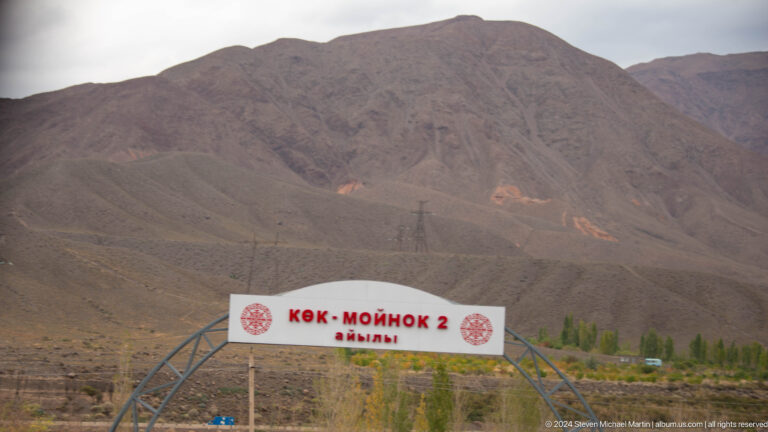 Roadside welcome sign before barren mountains.