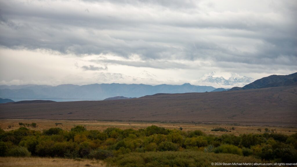 Open plain with shrubs beneath layered clouds.