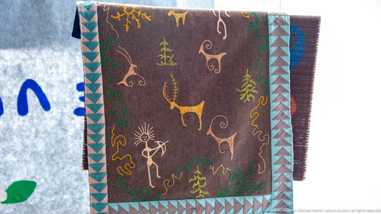 Embroidered textile with deer and symbolic motifs.