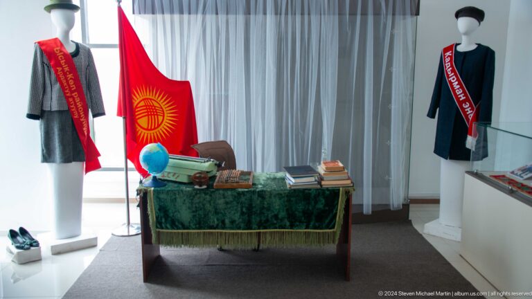 Museum display with kyrgyz flag and domestic objects.