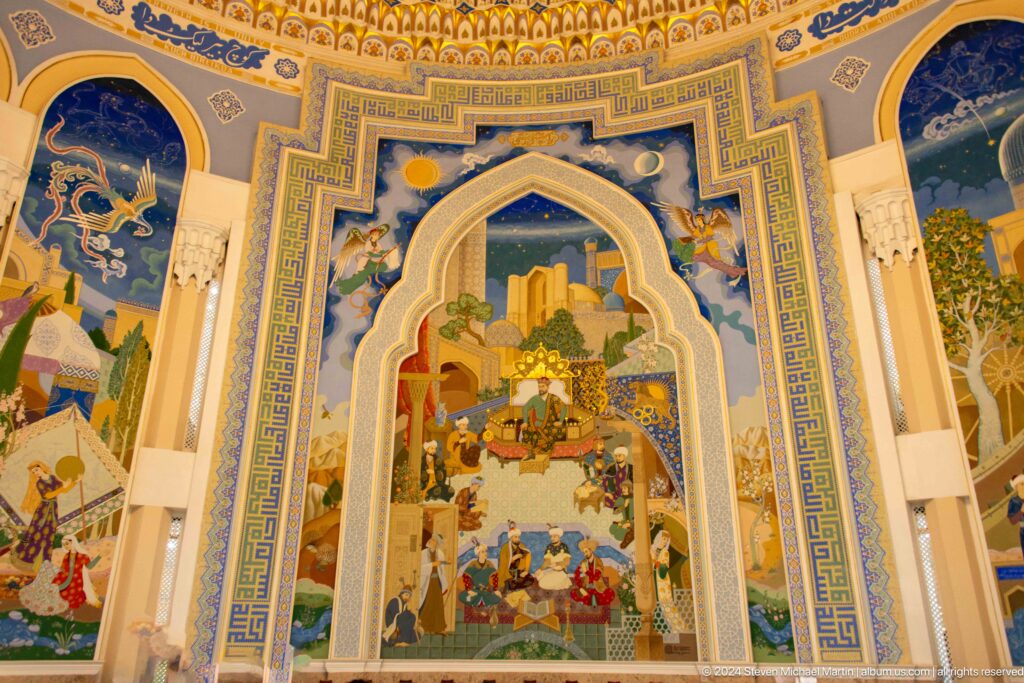 Large pointed-arch interior mural showing a courtly historical scene, city architecture, and ornate blue-and-gold borders.