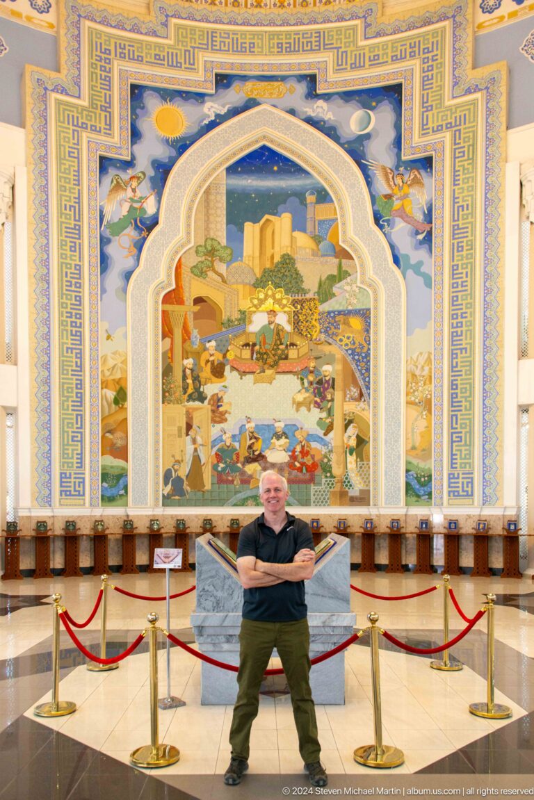 Smiling man with folded arms in front of the pointed-arch mural.