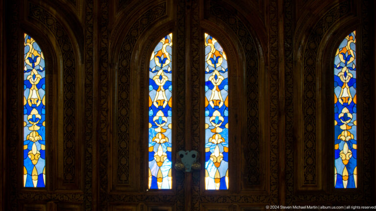 Dark carved doors with two narrow illuminated glass panels.