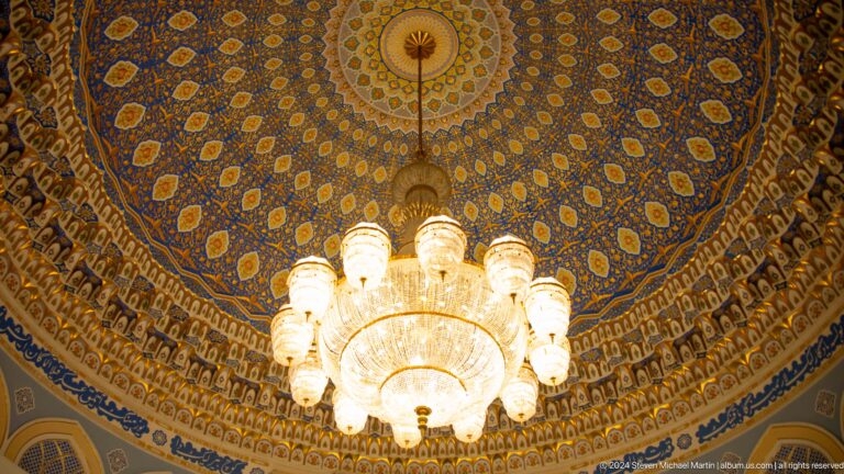 Bright chandelier suspended beneath densely patterned dome.