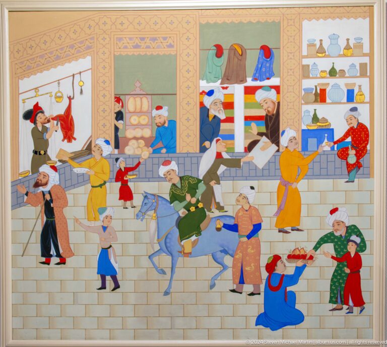 Busy street scene with shops, fabrics, food, and a pack animal.