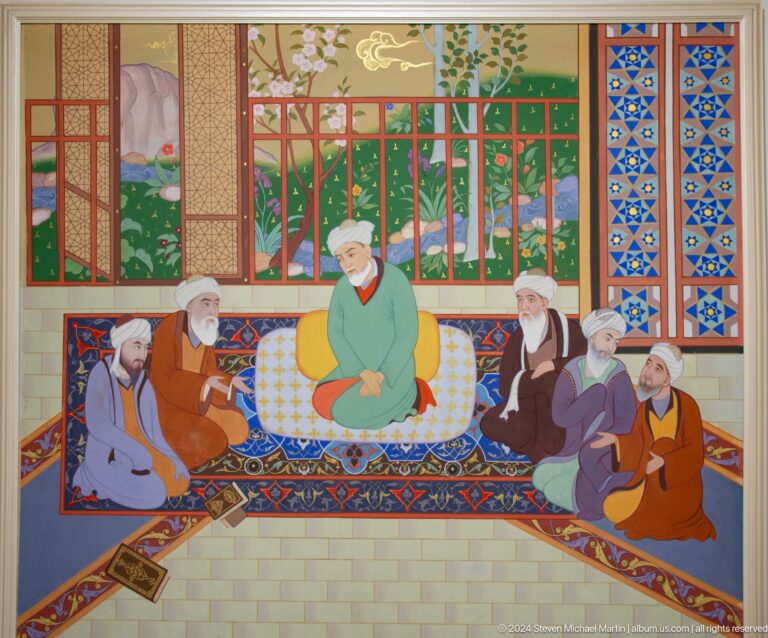 Central elder in green surrounded by seated men and books.