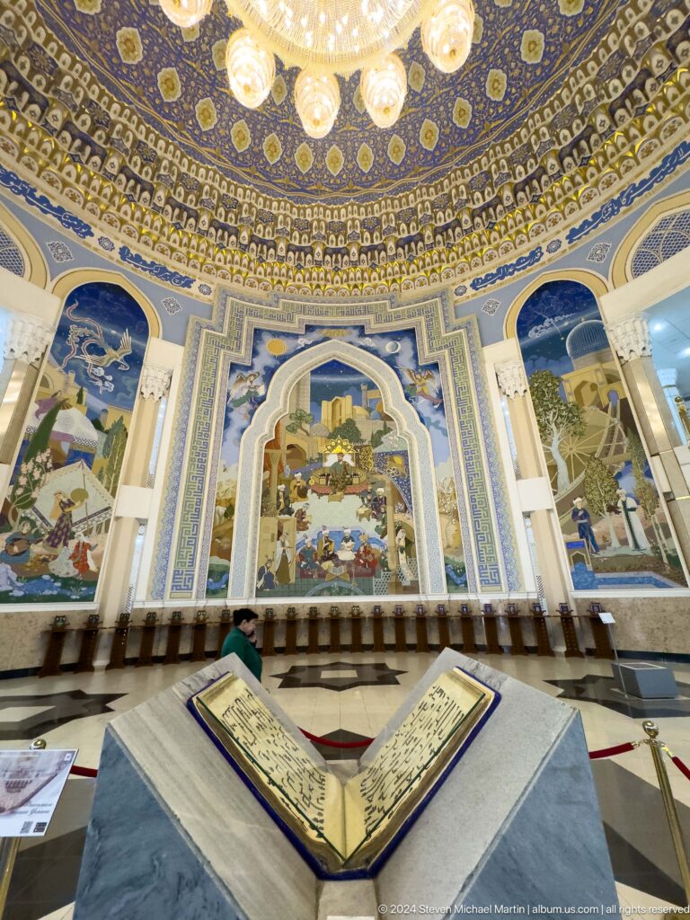 Open manuscript aligned with pointed-arch mural across the hall.