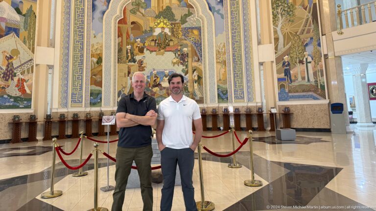 Two men standing side by side in front of the court mural.