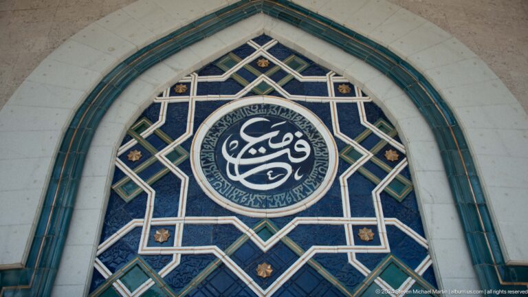 Close-up of a blue pointed-arch window with a large circular calligraphic medallion and interlocking white geometric tracery.