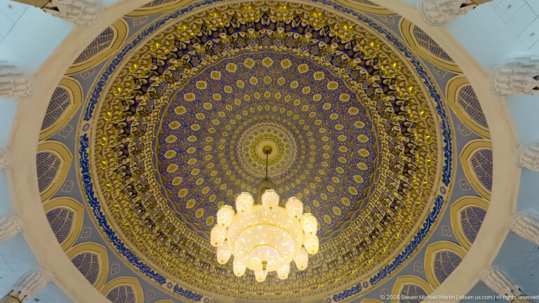 Entire blue-and-gold dome framed by windows and chandelier.