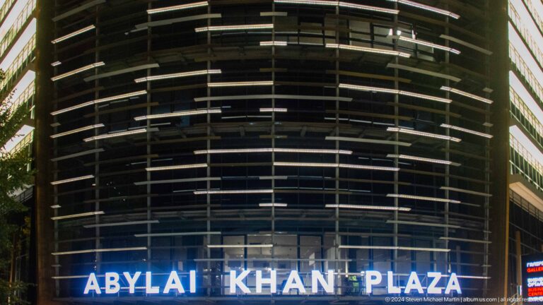 Night view of the illuminated ARYAL KHAN PLAZA sign on a curved glass building exterior in Almaty, Kazakhstan.