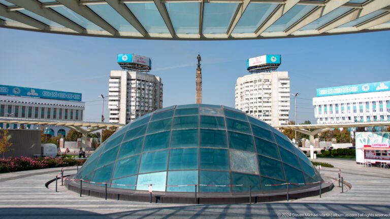 Glass dome structure in Republic Square with tall modern buildings in the background in Almaty.