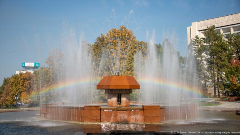 Circular park fountain in Almaty with water spraying around a central kiosk structure.