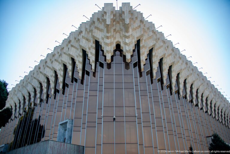 Dramatic concrete facade of the Abai Palace of the Republic in Almaty, with white hanging geometric forms along the upper edge.