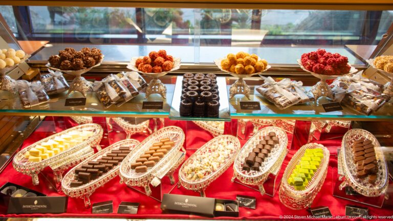 Glass display case in a market filled with rows of decorated pastries and sweets.